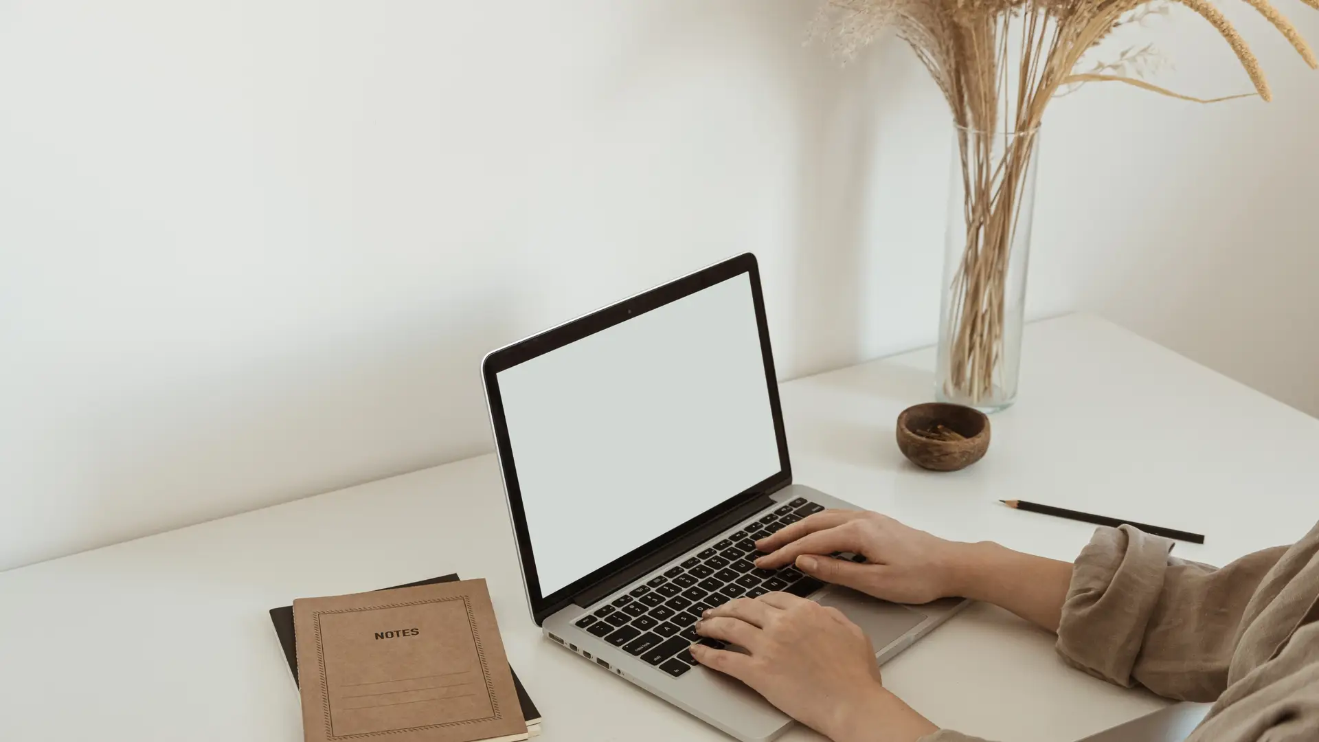 person typing on a laptop with a note pad beside